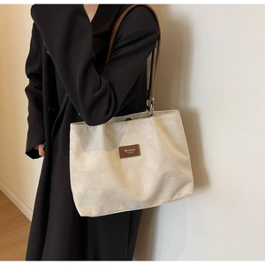 Detail of heart jacquard texture and brown leather logo patch on beige canvas tote bag