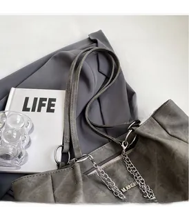 Detail of dark gray matte tote bag with silver chain strap and metal logo on fabric surface