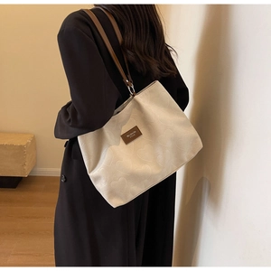 Detail of cream tote bag with heart-embossed texture and brown leather logo tag