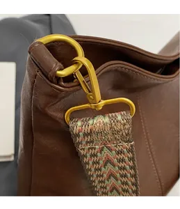 Detailed close-up of retro gold hardware hook and geometric woven strap on a brown tote bag