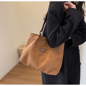 Detail of a brown suede tote bag with heart patterns and premium leather brand label