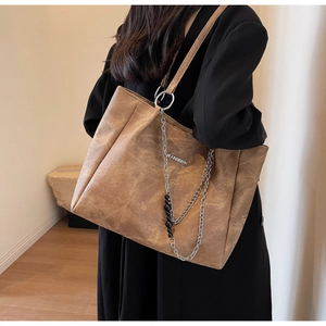 Detail of a large brown leather tote bag with metallic chain and beaded pendant