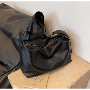 Détail de la texture cuir noir grainé et de l'anneau métallique doré sur le sac