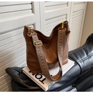 Detail of dark brown tote bag featuring retro ethnic woven shoulder strap and gold hardware
