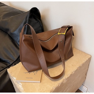 Détail du sac en cuir grainé marron avec boucle dorée sur un support en pierre minimaliste