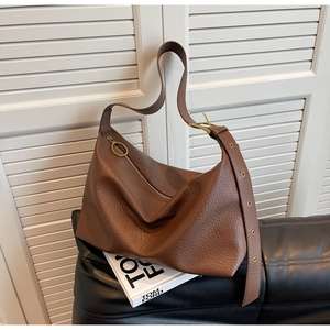 Détail du sac en cuir marron avec œillets dorés sur la bandoulière et fermeture éclair