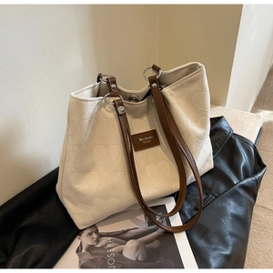 Detail of white heart-embossed tote bag with brown leather handles and magnetic closure