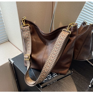 Detail of vintage brown leather hobo bag featuring a wide bohemian woven shoulder strap