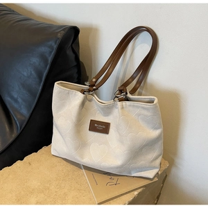 Detail of cream canvas tote featuring embossed heart patterns and brown leather handles