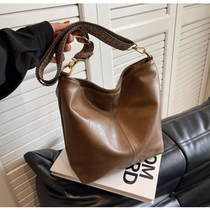 Close-up of brown faux leather bucket bag with retro patterned wide strap and gold hardware
