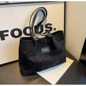 Close-up of black suede tote bag with embossed heart patterns and leather handles