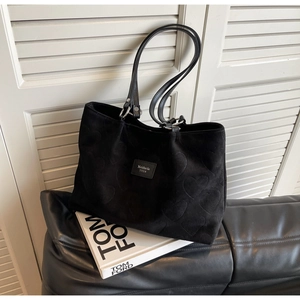 Macro detail of black tote bag featuring embossed heart patterns and leather brand label
