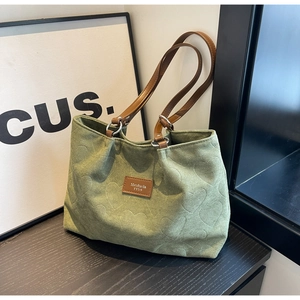 Detail of green canvas tote featuring embossed heart patterns and brown leather strap