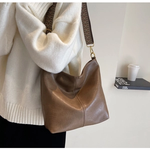 Close-up of brown leather hobo bag with vintage texture and colorful woven shoulder strap
