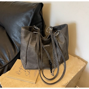 Detail of suede tote bag featuring metallic chain, logo plaque and sturdy side D-ring buckle