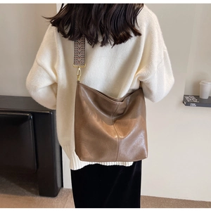 Brown leather bucket bag with geometric woven strap shown on model for size perspective