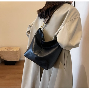Detail of a large black leather bucket bag featuring a wide jacquard woven shoulder strap