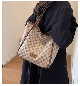 Detail of large beige tote bag with brown monogram pattern and fashion metal plaque