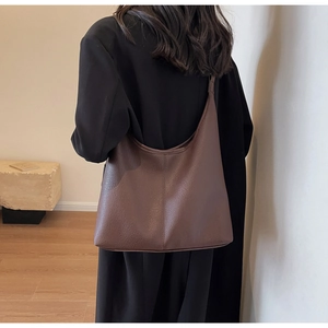 Deep brown pebble leather bucket bag shown on shoulder over a black wool coat