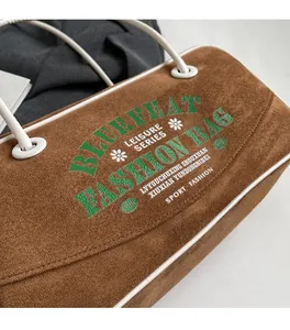 Détail de la texture suédine marron avec impression de lettres vertes et blanches sur le sac