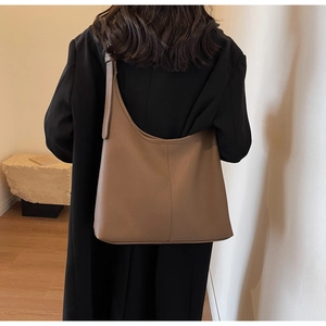 Rear view of a model wearing a large khaki hobo bucket bag with a wide adjustable strap