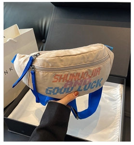 Beige crossbodytas met pixeltekst en blauwe riem gepresenteerd in een geschenkdoos