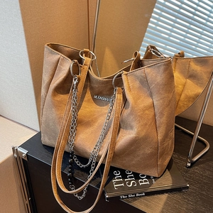 Large brown suede tote bag with metal chain detail shown in a minimalist warm setting