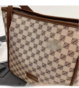 Detail of beige logo fabric and brown leather trim on a large fashion tote bag