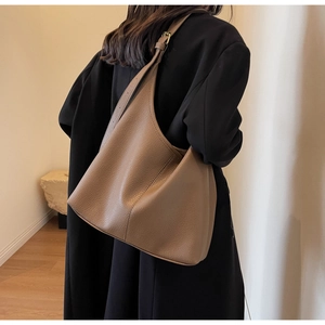 Brown litchi grain leather hobo bag worn by model over a black winter coat in a room
