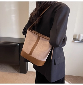 Detail view of large beige canvas bucket bag with brown leather trim worn by model