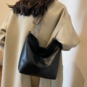 Large black hobo bucket bag with ethnic woven strap and golden hardware on beige coat