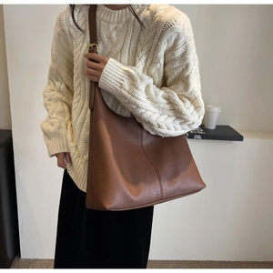 Detail of a large brown pebble leather tote bag with stylish vertical stitching and wide strap