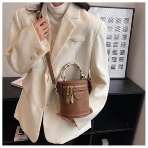 Gros plan d'un sac bandoulière cylindrique marron avec poignée en soie et boucles dorées