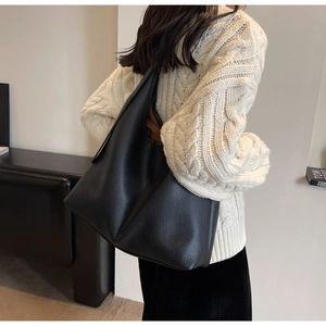 Close-up of black lychee grain leather tote bag worn by model in cozy winter sweater