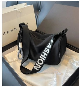 Detail of black crescent bag featuring wide FASHION logo strap and woven rope charm