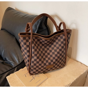 Detail of checkered tote bag with double handles and fashion logo on natural stone