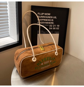 Gros plan d'un sac cylindre en daim marron avec fermetures éclair dorées et sangles