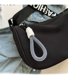 Detail of black crescent bag featuring a white FASHION letter strap and woven zipper pull