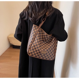 Detailed view of a large brown checkerboard tote bag worn by a model in a minimal setting