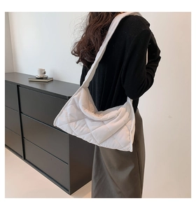 Détail d'un sac à bandoulière matelassé blanc doux porté par un mannequin en studio minimaliste