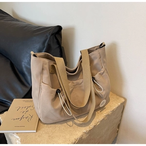Detail der khakifarbenen Canvas-Tragetasche mit Tunnelzugtaschen und besticktem Aufnäher