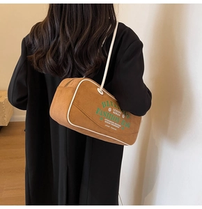 Gros plan d'un sac porté épaule en daim marron avec texte vert et détails zippés