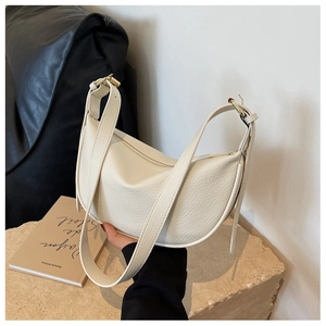 Gros plan du sac demi-lune blanc cassé à texture grainée sur socle en pierre