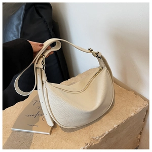 Détail d'un sac demi-lune crème en cuir grainé avec des finitions métalliques dorées