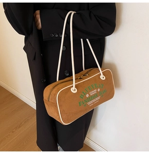 Détail d'un sac à bandoulière en daim marron avec fines bretelles et lettrage graphique