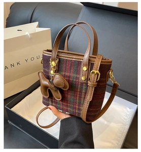 Détail d'un sac seau vintage à carreaux avec anses en cuir et breloque petit chien