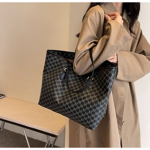 Detail of black monogram tote bag with gold hardware worn with a classic beige coat
