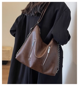 Detail of vintage brown leather bag with silver zippers and chain strap on a black coat