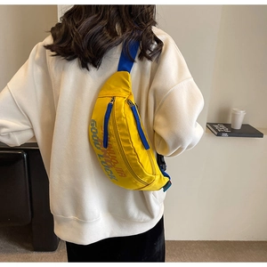 Detail van gele nylon borsttas met Good Luck tekst en blauwe riem op een wit sweatshirt