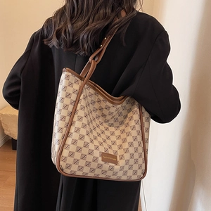 Large vintage monogram tote bag with leather straps worn over a black winter coat